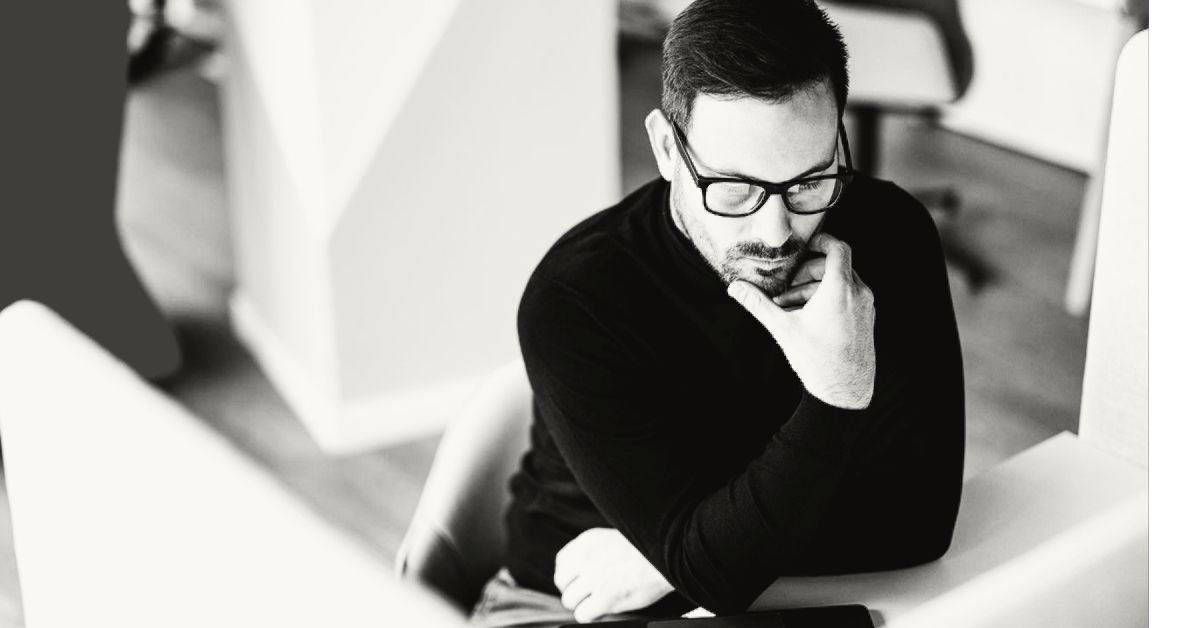 Black and white image of man thinking in front of screens